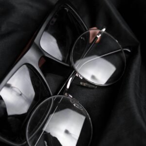 Close-up of modern eyeglasses and sunglasses resting on black fabric, featuring reflections.