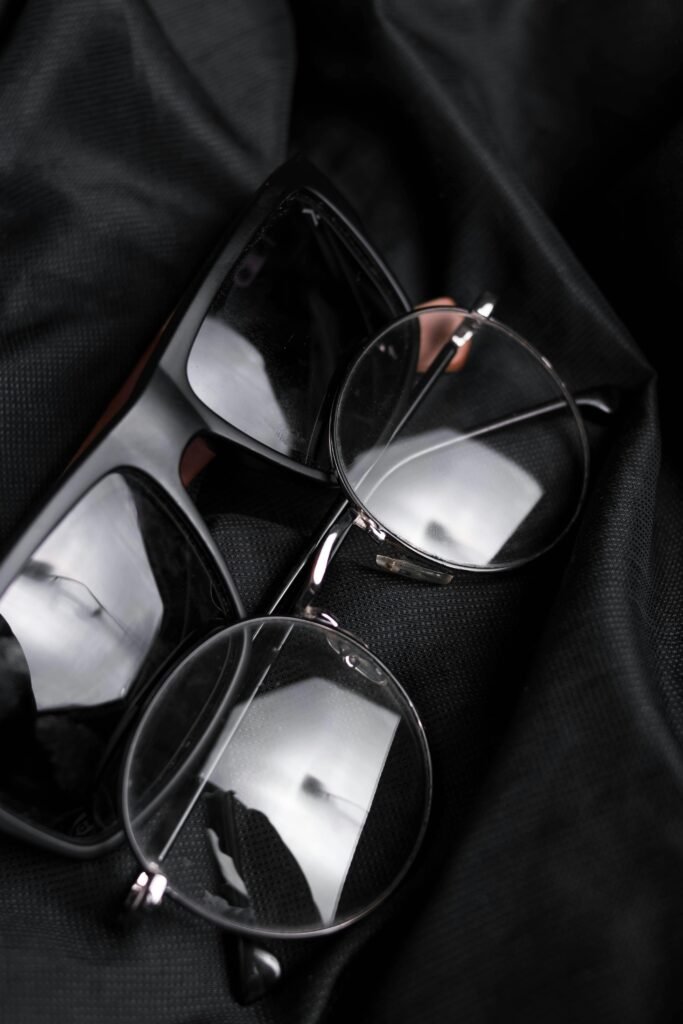 Close-up of modern eyeglasses and sunglasses resting on black fabric, featuring reflections.