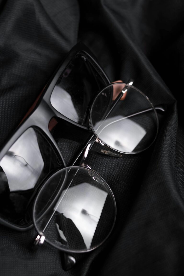 Close-up of modern eyeglasses and sunglasses resting on black fabric, featuring reflections.